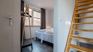 A bedroom with a bed, a wooden ladder, and a window with curtains. - Nice Apartment on Ameland With Balcony/terrace (Buren)