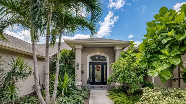 A residential house with a front entrance, a pathway leading to the door, and various tropical plants around.