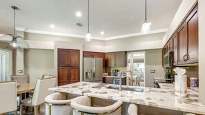 A modern kitchen with a marble island, bar stools, wooden cabinets, and stainless steel appliances.