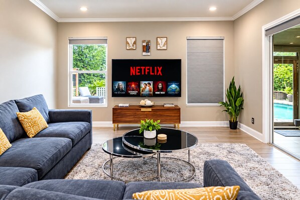 A modern living room with a grey sofa, a coffee table, and a flat-screen TV displaying Netflix content. - Private Oasis: Heated Pool & Sauna (Riverview)