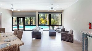 A spacious living area with a pool view, wicker furniture, ceiling fans, and a kitchen counter.