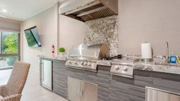 An outdoor kitchen with a grill, a sink, and a television mounted on the wall.