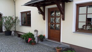 A building with a wooden door, a window, and a small porch area with potted plants. - Sachon Comfortable Holiday Residence (Nebelschütz)