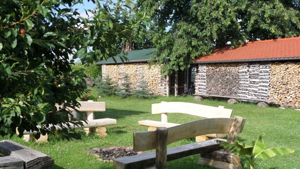 A stone building with a green roof, surrounded by a grassy area with wooden benches and a tree. - Sachon Comfortable Holiday Residence (Nebelschütz)