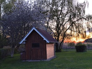 A small wooden shed with a pitched roof, surrounded by grass and trees. - Familienfreundliche Haushaelfte in Alt Bukow (Alt Bukow)