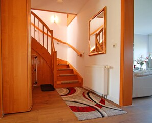 A wooden staircase with a handrail, a white radiator, and a patterned rug on a wooden floor. - Familienfreundliche Haushaelfte in Alt Bukow (Alt Bukow)
