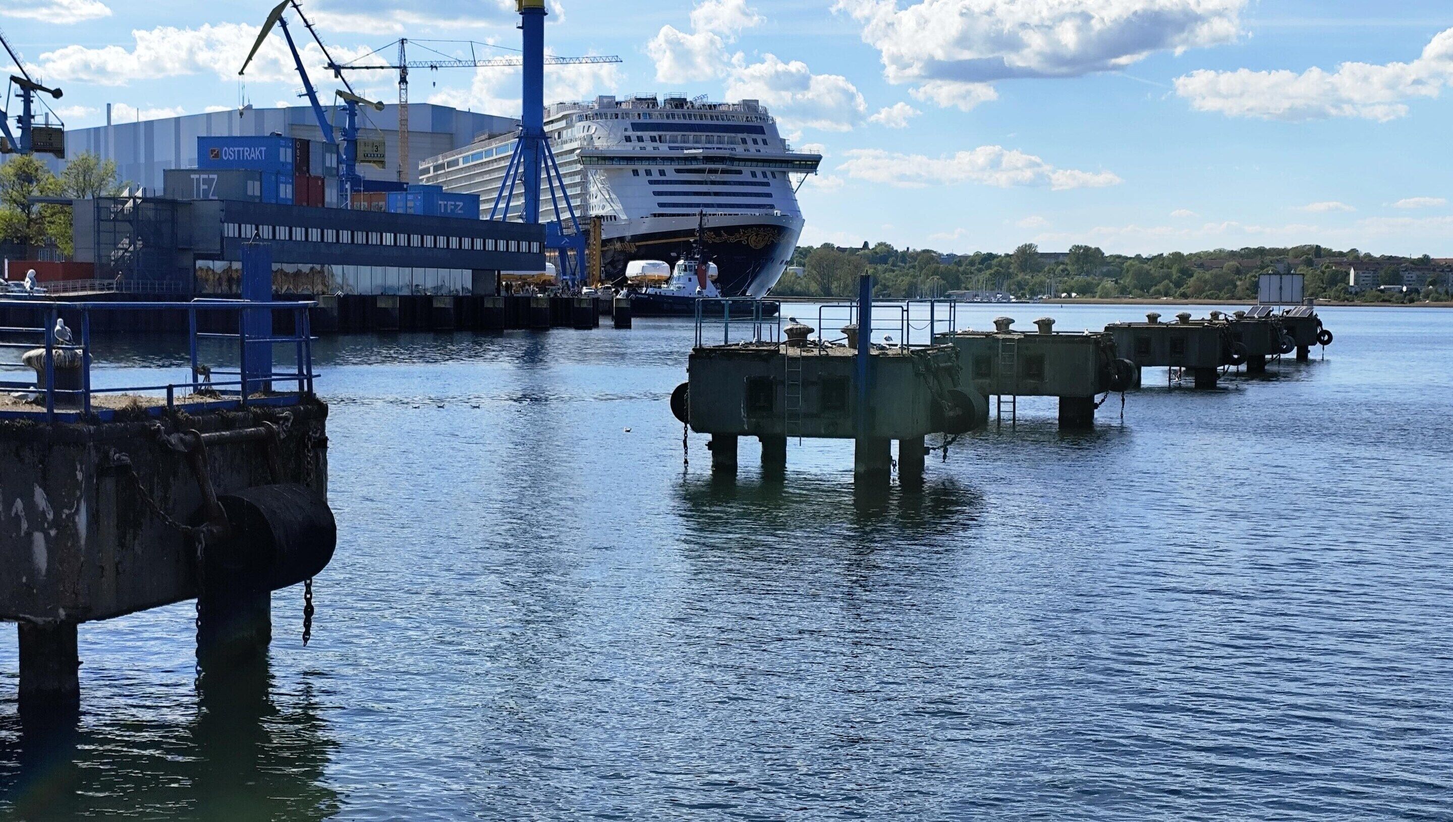 Ein Schiff liegt im Hafen vor dem Hintergrund von Industriegebäuden und Kränen.