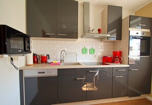 A modern kitchen with dark cabinets, a microwave, a coffee maker, and a dishwasher. - Familienfreundliche Haushaelfte in Alt Bukow (Alt Bukow)