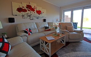 A living room with a sofa, armchair, coffee table, and artwork on the wall. - Familienfreundliche Haushaelfte in Alt Bukow (Alt Bukow)