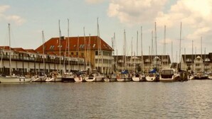 A marina with multiple boats docked, a building with a red roof, and a clear sky with clouds. - Beach Dune 12 on the Beach (Karlshagen)