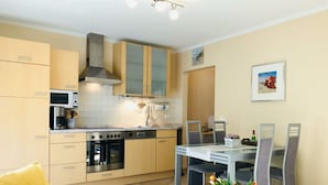 A compact kitchen with modern appliances, a dining area with a glass table, and a sofa with a yellow pillow. - Beach Dune 12 on the Beach (Karlshagen)