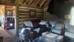 A rustic log cabin interior with a leather couch, a white armchair, a wooden coffee table, and a chandelier. - Best Mountain View in Utah. Rustic ranch setting.  (Provo)