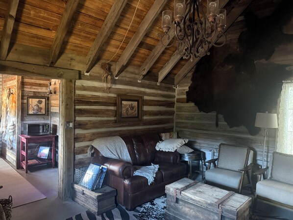 A rustic log cabin interior with a leather couch, a white armchair, a wooden coffee table, and a chandelier. - Best Mountain View in Utah. Rustic ranch setting. (Provo)