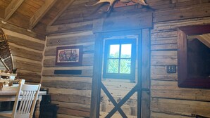 A rustic log cabin interior with a wooden ceiling, a chandelier, a large antler decoration, a wooden door, and a zebra-patterned rug. - Best Mountain View in Utah. Rustic ranch setting.  (Provo)