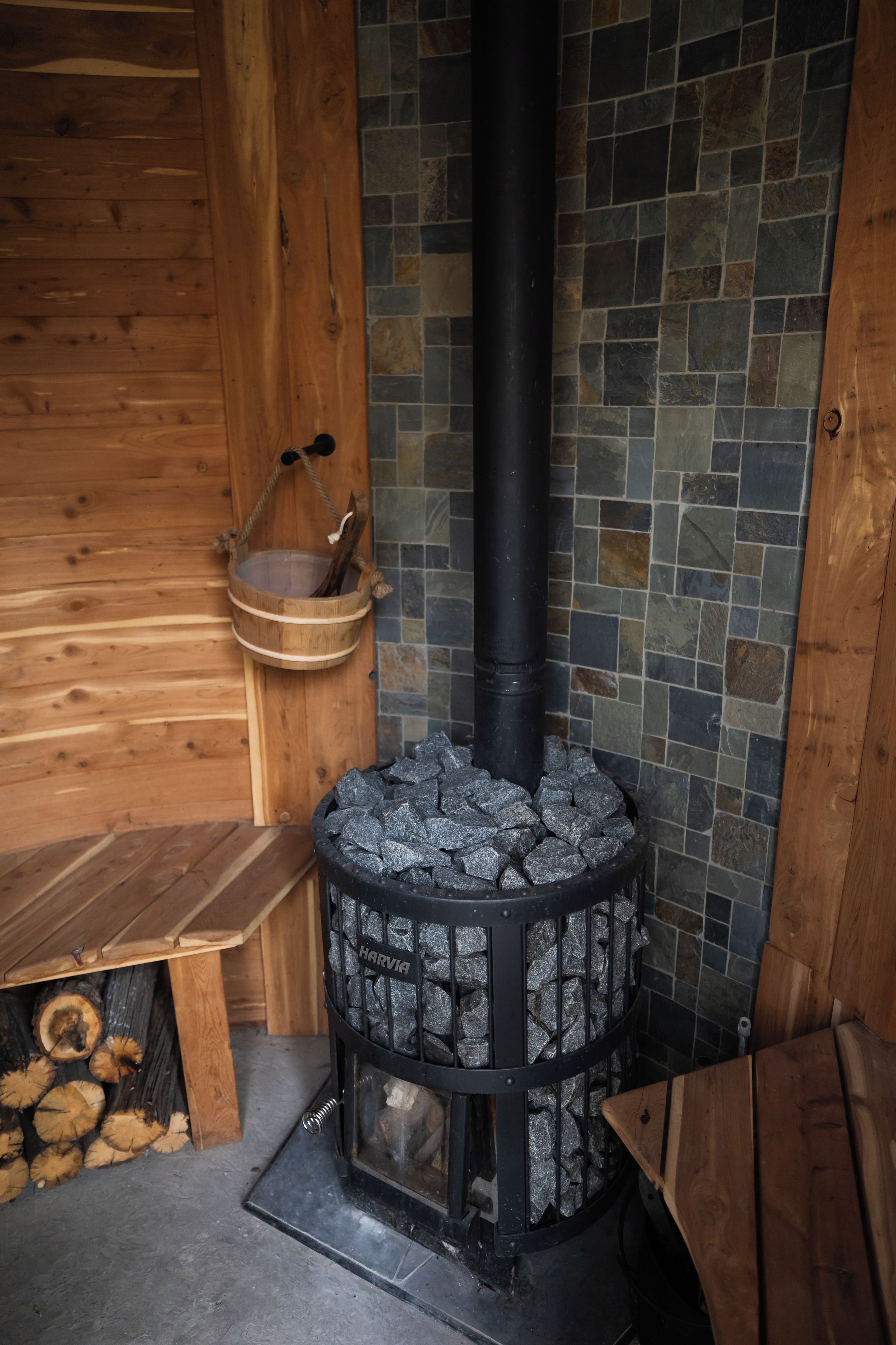 A wood-burning stove with a stone surround, a wooden bench, and a hanging basket.