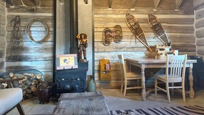 A rustic cabin interior with a wood-burning stove, wooden walls, a dining table with chairs, and various decorative items including antlers and a rooster statue. - Best Mountain View in Utah. Rustic ranch setting. (Provo)