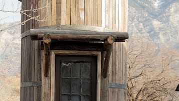 A rustic wooden structure with a dark brown door, a stone base, and a log pile beside it.