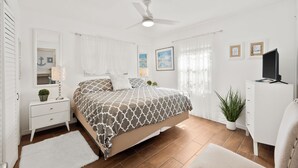 Une chambre à coucher comprenant un lit, une table de chevet, une commode, un ventilateur de plafond et une plante en pot.
