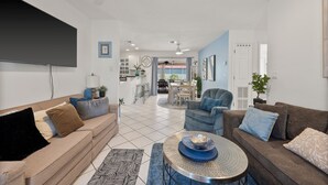 Un salon moderne avec un canapé, un fauteuil et une table basse. On aperçoit à l’arrière-plan un coin repas avec une table et des chaises.