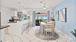 Une cuisine moderne avec des meubles blancs, un coin repas doté d’une table et de chaises en bois, et une vue sur l’extérieur grâce à une porte vitrée.