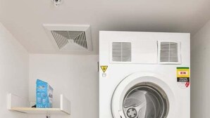 Una lavanderia compatta con lavatrice e asciugatrice Bosch, un lavandino piccolo e un sistema di ventilazione.