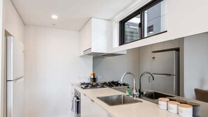 Una cucina moderna con mobili bianchi, un fornello a gas, un lavello e una finestra sopra il piano di lavoro.