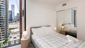 Una moderna camera d'albergo con un letto grande, un comodino rotondo, uno specchio e vista sulla città attraverso un'ampia finestra.