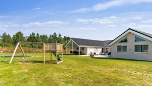 A single-story house with a covered patio, a swing set, and a trampoline in the yard. - 5 Star Holiday Home in Norre Nebel (Norre Nebel)