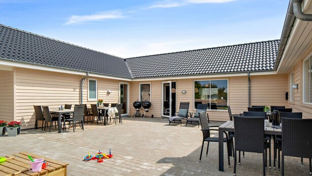A covered outdoor patio with tables and chairs, a barbecue grill, and a wooden playset. - 5 Star Holiday Home in Norre Nebel (Norre Nebel)