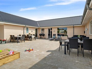 A covered outdoor patio with tables and chairs, a barbecue grill, and a wooden playset.