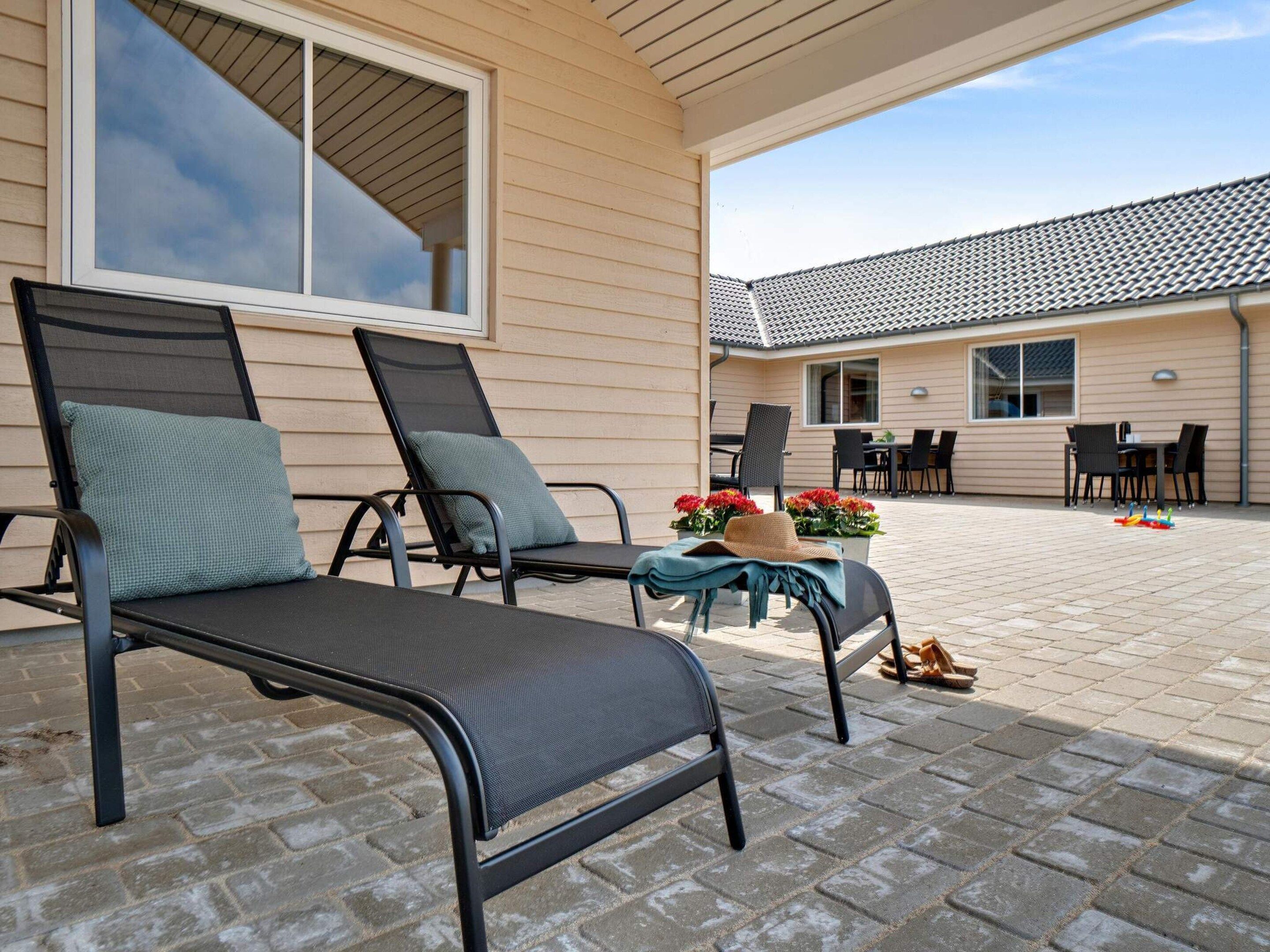 A patio area with two lounge chairs, a table with flowers, and a view of a building with a tiled roof.