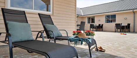 A patio area with two lounge chairs, a table with flowers, and a view of a building with a tiled roof.