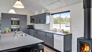 A modern kitchen with a central island, stainless steel appliances, and a wood-burning stove. - 5 Star Holiday Home in Norre Nebel (Norre Nebel)