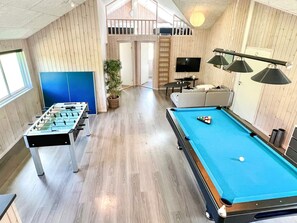 A room with a foosball table, a pool table, a sofa, a TV, and a staircase leading to an upper level. - 5 Star Holiday Home in Norre Nebel (Norre Nebel)