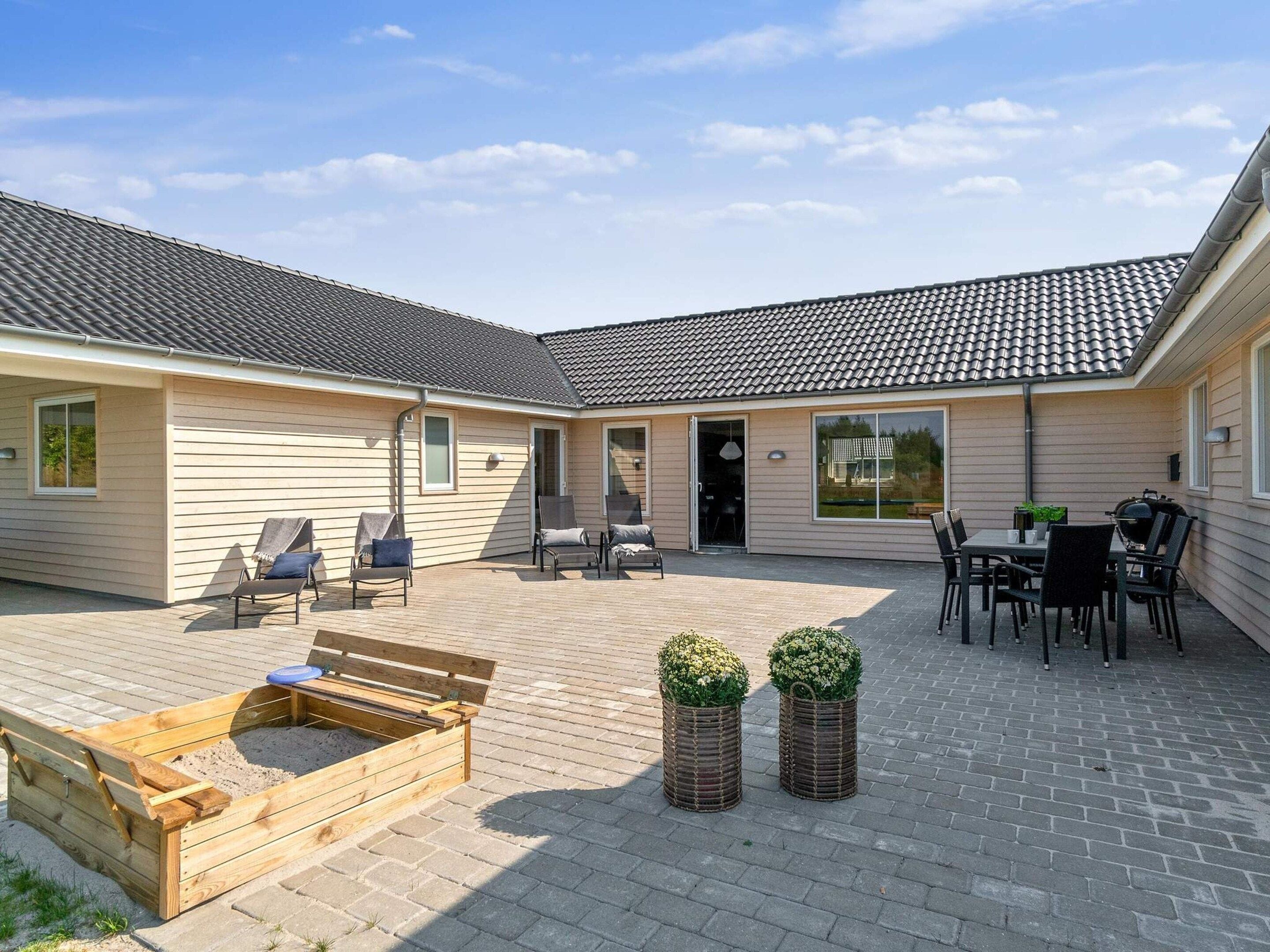 Un patio couvert avec une terrasse en bois, des sièges d’extérieur et un barbecue.