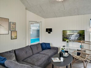 A living room with a grey sofa, a coffee table, a wicker chair, a TV, and a glass door leading to a pool.