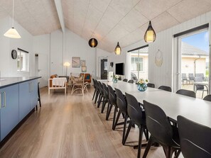 A spacious kitchen with a long dining table, modern pendant lights, and a view to the outside. - 5 Star Holiday Home in Norre Nebel (Norre Nebel)