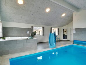 A swimming pool area with a hot tub, a slide, and a view of the outside.