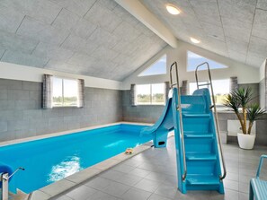 An indoor swimming pool with a blue slide, a lifeguard chair, and a potted plant. - 5 Star Holiday Home in Norre Nebel (Norre Nebel)