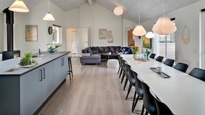 A modern kitchen with a central island, dining area with a long table and chairs, and a cozy seating area with a sofa. - 5 Star Holiday Home in Norre Nebel (Norre Nebel)