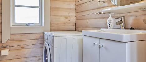 A compact bathroom with wooden paneling, a washing machine, a sink with a mirror, and a window.
