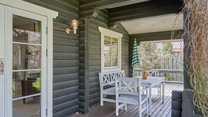 Une terrasse en bois avec une table et des chaises blanches, un luminaire suspendu et une vue sur l’extérieur.