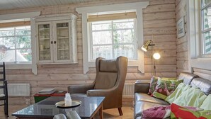 L’intérieur chaleureux d’un chalet avec un fauteuil en cuir, un canapé agrémenté de coussins colorés, un meuble en bois et une table sur laquelle se trouve une bouteille.