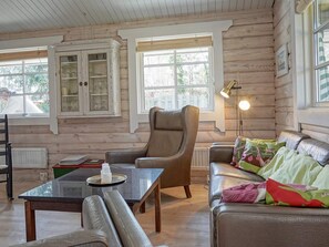 Een gezellig interieur van een blokhut met een leren fauteuil, een bank met kleurrijke kussens, een houten kast en een tafel met een fles.