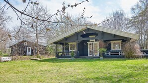 Un chalet rustique doté d’un porche, entouré d’une cour verdoyante et d’arbres sans feuilles.