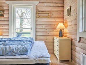 Une chambre à coucher avec un lit, une table de chevet avec une lampe, un mur en bois et une fenêtre.