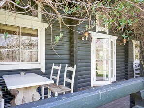 Une cabane en bois avec une véranda, une table et deux chaises.