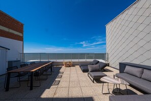 A rooftop terrace with a long wooden table, multiple chairs, a sofa, and a small seating area. - Beautiful Penthouse With Phenomenal sea View (Middelkerke)