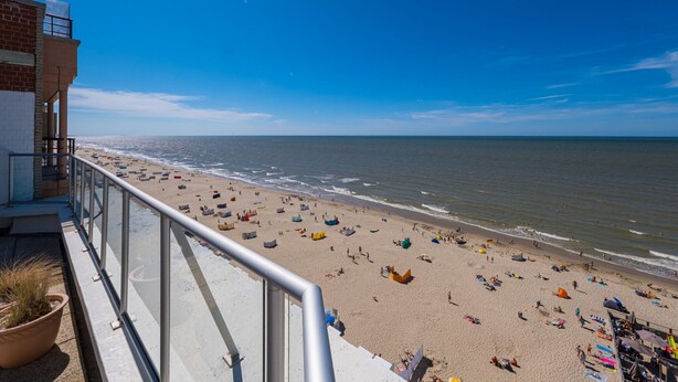 A beach with a clear view of the ocean, a building with a balcony, and a railing.