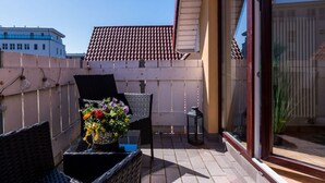 A balcony with wicker furniture, a potted plant, and a view of a building with a tiled roof. - Holiday Apartment in Otseebad Wustrow (Ostseebad Wustrow)
